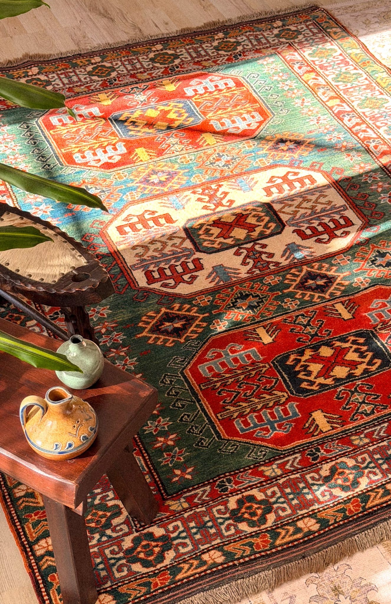 Hand-knotted Kazak rug in red, green and cream with a wooden stool and ceramics